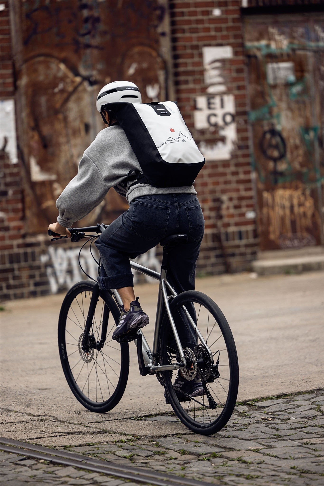 Frau sitzt auf Metalltreppe mit ORTLIEB Velocity Design Rucksack in weiß-schwarz mit roter Sonne